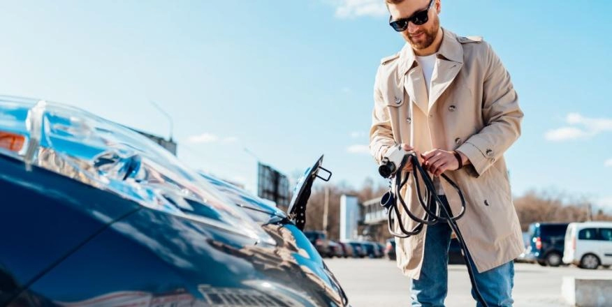 Man holds charging cable in front of EV bonnet