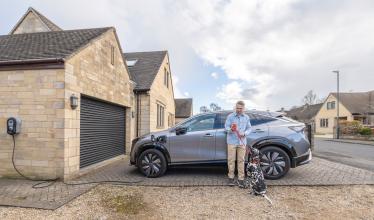 Home charge point charging EV next to man using Zapmap app on phone holding leash of Dalmation dog